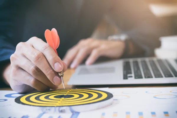 Main tenant une fléchette visant une cible sur un graphique, symbolisant la définition d’objectifs et la stratégie marketing