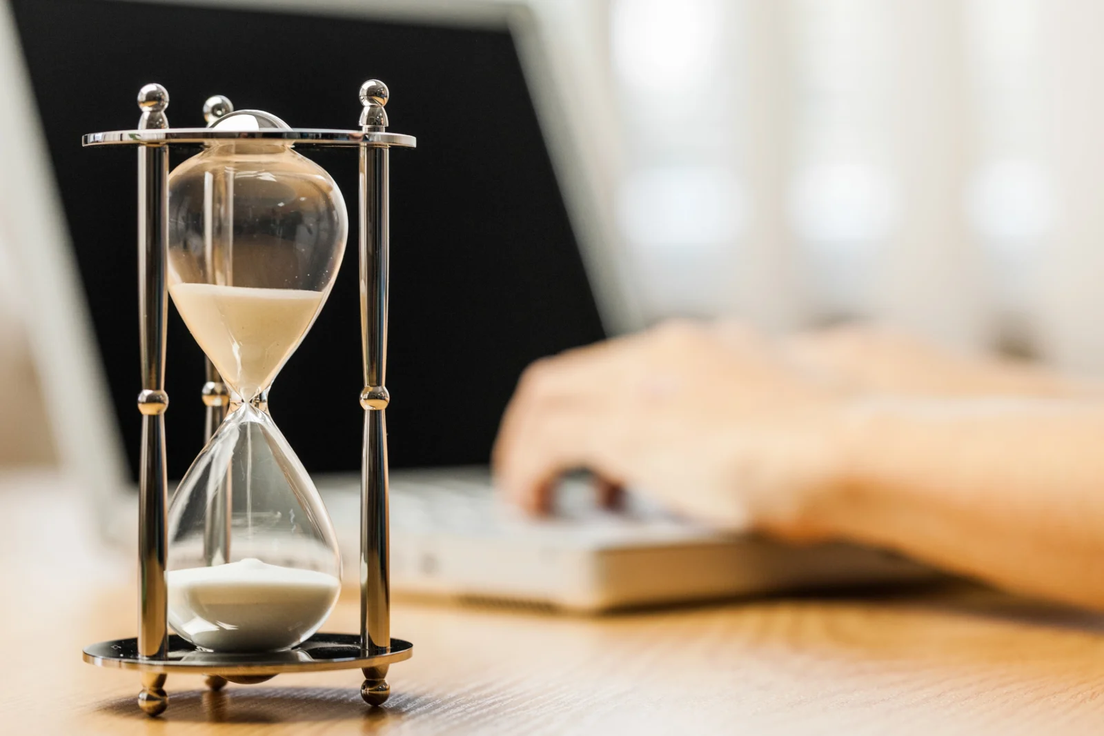 closeup hourglass with person typing laptop background