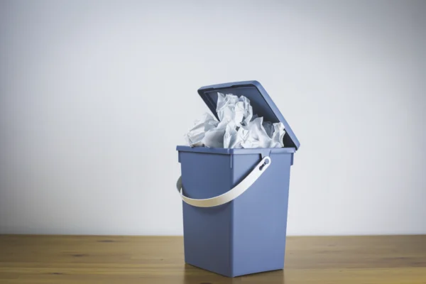 Corbeille remplie de feuilles de papier froissées sur un bureau, illustrant la suppression de documents, la gestion des déchets papier et l’optimisation des processus en entreprise