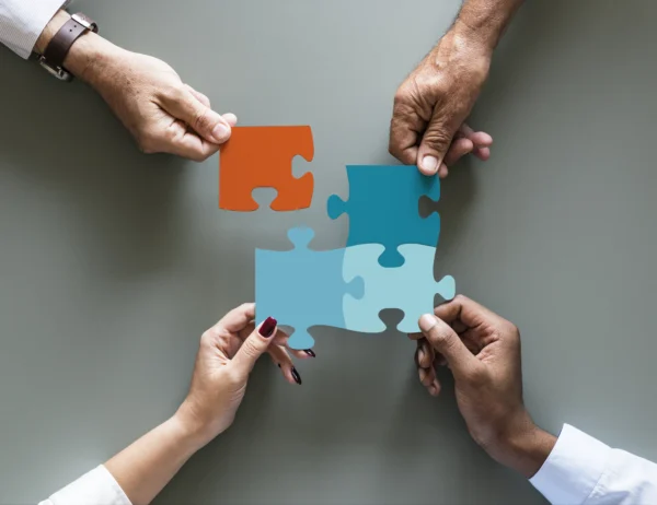 Plusieurs mains assemblant des pièces de puzzle colorées, illustrant la collaboration, l’intégration de solutions et l’interconnexion des systèmes en entreprise