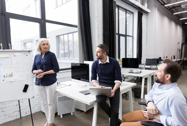 Équipe en réunion dans un bureau moderne avec présentation sur tableau et ordinateur portable, illustrant la collaboration et le pilotage de projet en entreprise