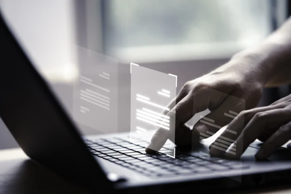 Main utilisant un ordinateur portable avec documents numériques en surimpression, illustrant la gestion électronique des documents, la digitalisation et le traitement des données en entreprise