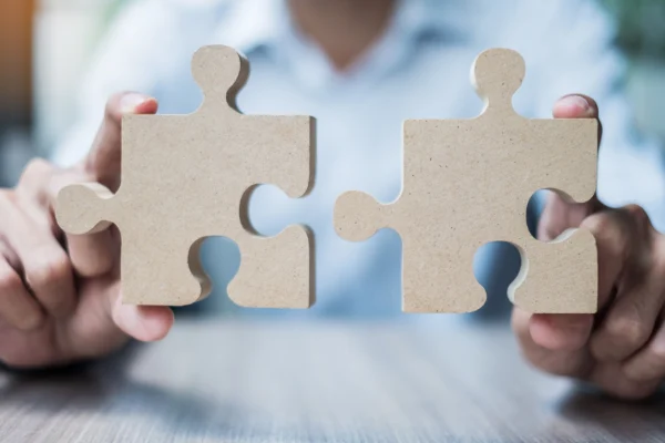 Deux mains rapprochant des pièces de puzzle en bois pour les assembler, symbolisant l’intégration de solutions, la collaboration et l’interconnexion des systèmes en entreprise